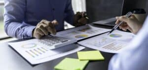 Business and partnership discussing using calculator to review balance sheet annual with holding pen